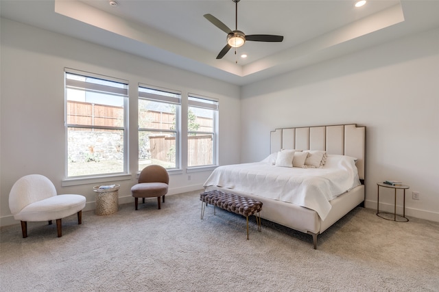 carpeted bedroom with ceiling fan and a tray ceiling