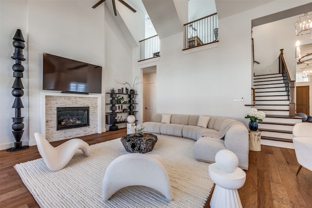 living room with a tiled fireplace, hardwood / wood-style floors, ceiling fan with notable chandelier, and a high ceiling