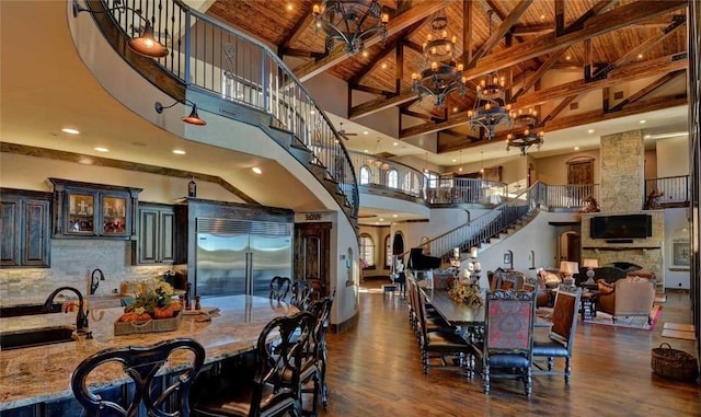 dining space with sink, an inviting chandelier, high vaulted ceiling, a fireplace, and dark hardwood / wood-style flooring