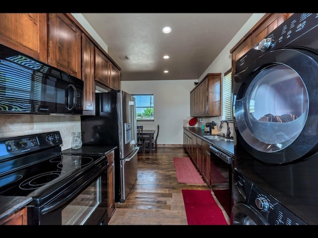 kitchen featuring sink, dark wood-type flooring, stacked washing maching and dryer, backsplash, and black appliances