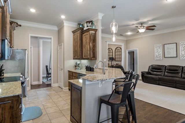 kitchen with pendant lighting, sink, stainless steel appliances, light stone countertops, and kitchen peninsula