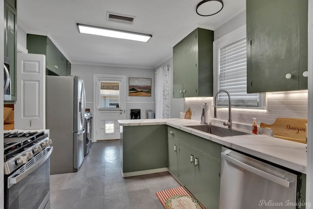 kitchen with appliances with stainless steel finishes, tasteful backsplash, ornamental molding, sink, and green cabinetry