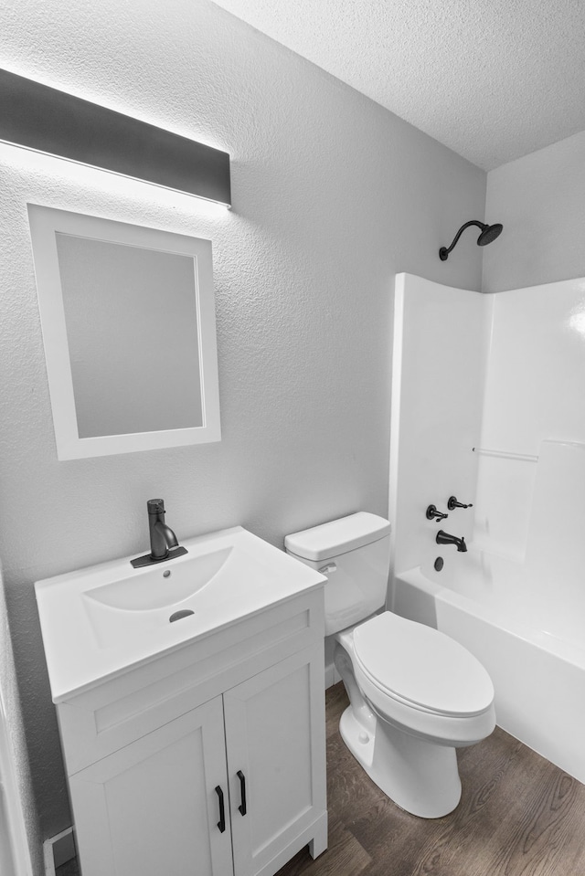 full bathroom with vanity, washtub / shower combination, hardwood / wood-style flooring, toilet, and a textured ceiling