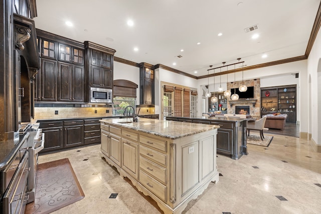 kitchen with appliances with stainless steel finishes, ornamental molding, dark brown cabinets, cream cabinets, and a center island with sink