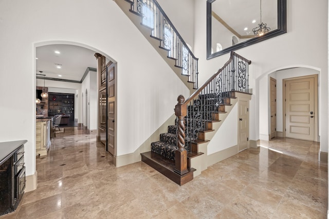 stairs featuring crown molding, a high ceiling, and an inviting chandelier