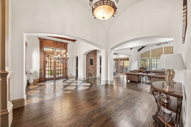 foyer with french doors, ceiling fan with notable chandelier, dark hardwood / wood-style floors, and high vaulted ceiling