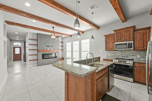 kitchen featuring an island with sink, sink, a large fireplace, hanging light fixtures, and stainless steel appliances