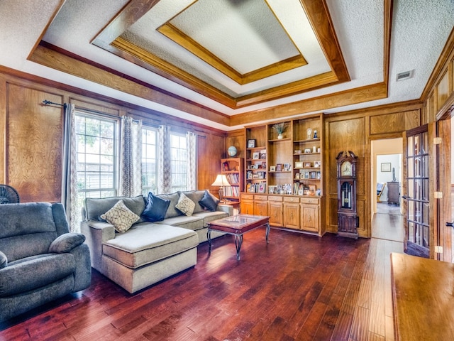 living room with dark wood-type flooring, a raised ceiling, built in features, wood walls, and a textured ceiling