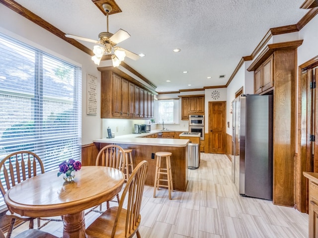 kitchen with ceiling fan, stainless steel appliances, kitchen peninsula, crown molding, and a textured ceiling