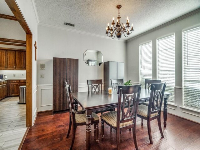 dining area with a chandelier, wood-type flooring, a textured ceiling, and ornamental molding