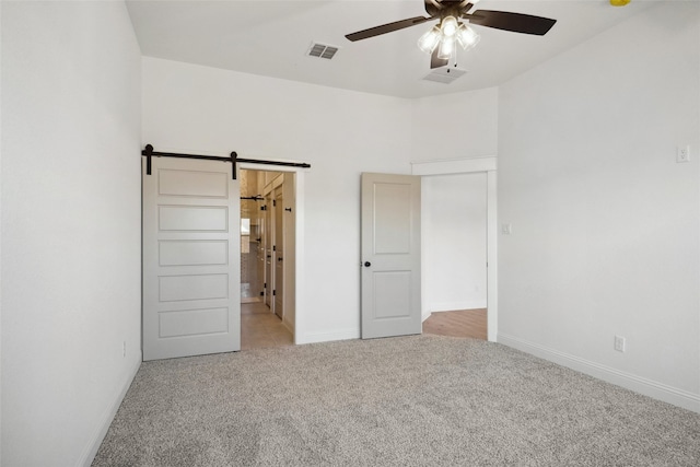 unfurnished bedroom featuring light colored carpet and a barn door