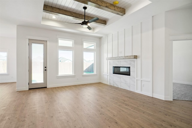 unfurnished living room featuring beamed ceiling, ceiling fan, a tiled fireplace, and light hardwood / wood-style flooring