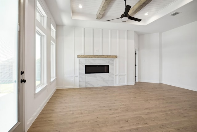 unfurnished living room with beam ceiling, a tile fireplace, light hardwood / wood-style floors, and ceiling fan