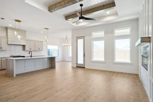 kitchen with ceiling fan with notable chandelier, decorative light fixtures, tasteful backsplash, an island with sink, and light wood-type flooring