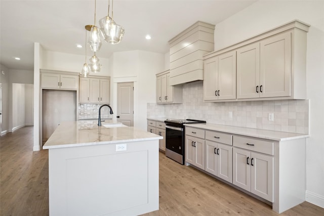 kitchen featuring sink, stainless steel range with electric stovetop, decorative light fixtures, light hardwood / wood-style flooring, and an island with sink