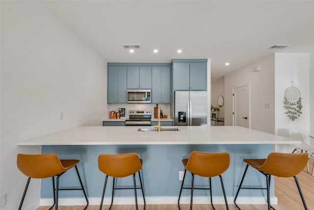 kitchen with sink, appliances with stainless steel finishes, a kitchen breakfast bar, kitchen peninsula, and light hardwood / wood-style floors