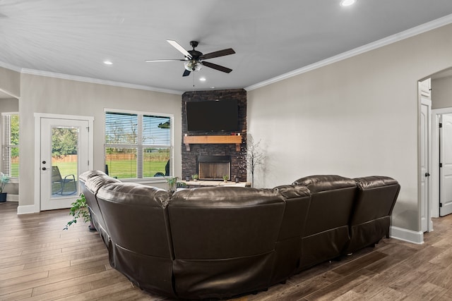 living room featuring ceiling fan, a stone fireplace, dark hardwood / wood-style flooring, and crown molding