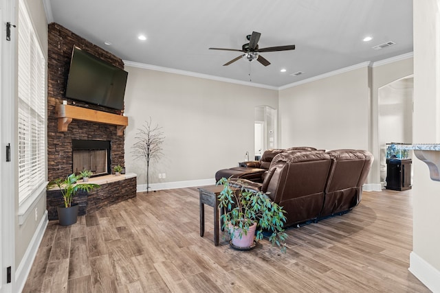 living room featuring ceiling fan, a stone fireplace, light wood-type flooring, and ornamental molding