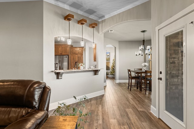 interior space with dark wood-type flooring, kitchen peninsula, decorative light fixtures, a kitchen bar, and stainless steel fridge with ice dispenser