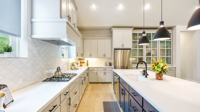 kitchen with appliances with stainless steel finishes, backsplash, decorative light fixtures, light hardwood / wood-style flooring, and white cabinets