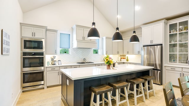 kitchen with a center island, hanging light fixtures, stainless steel appliances, a kitchen breakfast bar, and high vaulted ceiling