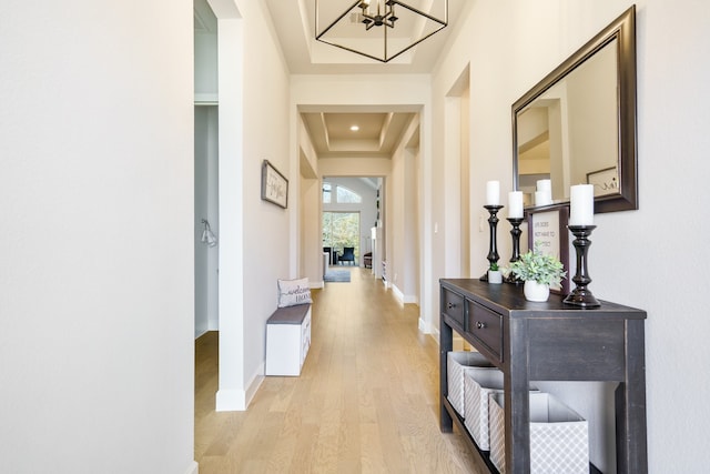 corridor featuring a tray ceiling, light hardwood / wood-style flooring, and an inviting chandelier