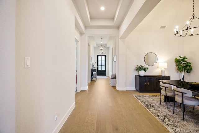 hall featuring a raised ceiling, a chandelier, and light wood-type flooring