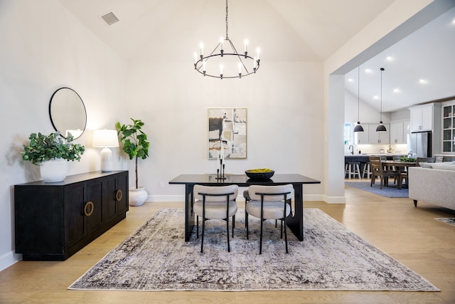 dining area featuring a chandelier, light wood-type flooring, high vaulted ceiling, and sink