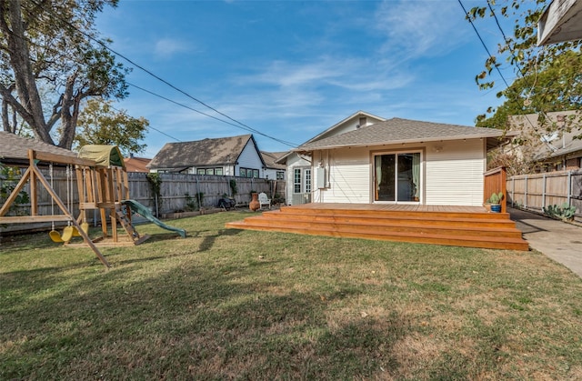 rear view of house with a wooden deck, a yard, and a playground