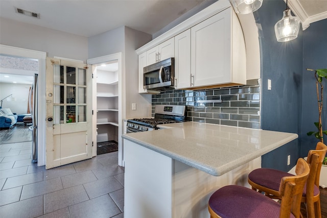 kitchen featuring pendant lighting, backsplash, white cabinets, a kitchen bar, and stainless steel appliances