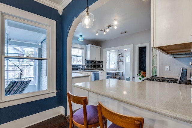 kitchen featuring decorative light fixtures, white cabinetry, dishwasher, sink, and a kitchen bar