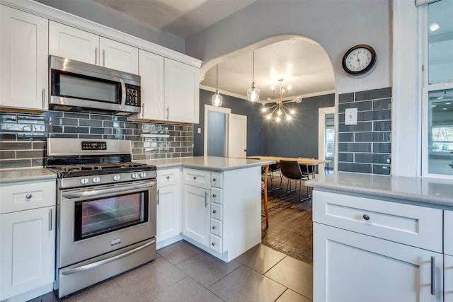 kitchen with decorative backsplash, appliances with stainless steel finishes, crown molding, decorative light fixtures, and white cabinetry