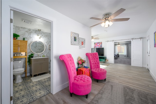 sitting room featuring a barn door, light hardwood / wood-style flooring, ceiling fan, and sink