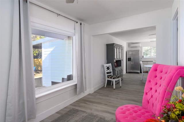 sitting room with hardwood / wood-style flooring, ceiling fan, a healthy amount of sunlight, and an AC wall unit