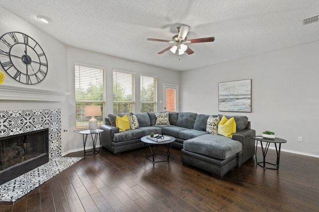 living room with a textured ceiling, dark hardwood / wood-style flooring, ceiling fan, and a tiled fireplace