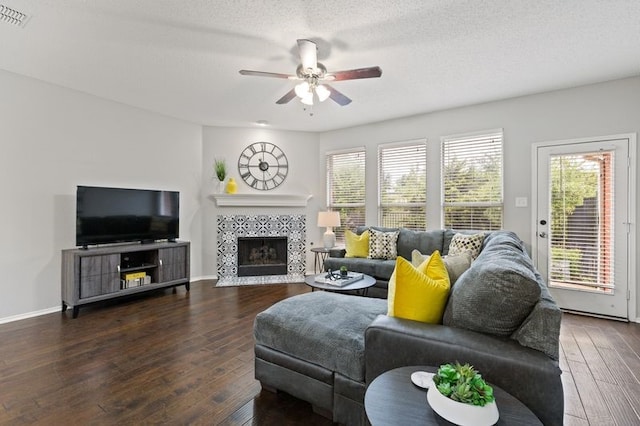 living room with a tiled fireplace, ceiling fan, a textured ceiling, and dark hardwood / wood-style flooring