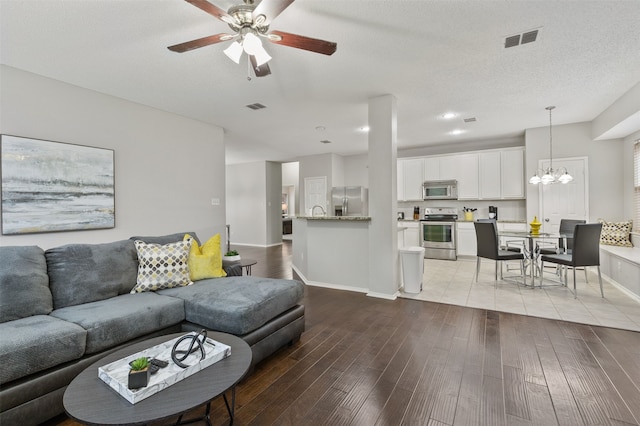 living room with ceiling fan with notable chandelier, a textured ceiling, and light hardwood / wood-style flooring