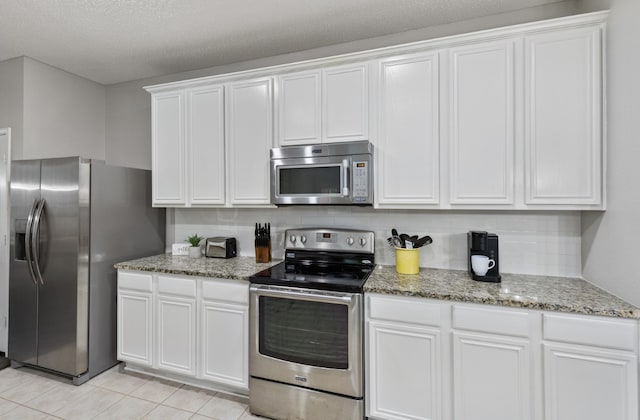 kitchen with white cabinetry, appliances with stainless steel finishes, light stone countertops, and light tile patterned floors