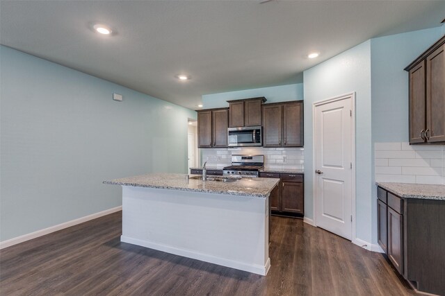 kitchen with a kitchen island with sink, dark hardwood / wood-style flooring, light stone counters, and appliances with stainless steel finishes