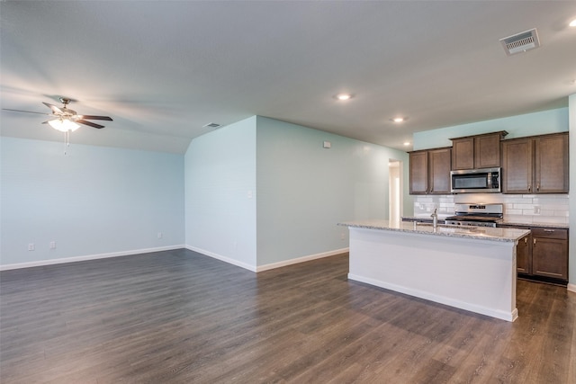 kitchen with appliances with stainless steel finishes, dark hardwood / wood-style flooring, tasteful backsplash, ceiling fan, and a center island with sink