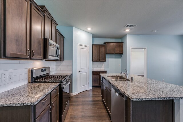 kitchen featuring sink, dark wood-type flooring, stainless steel appliances, backsplash, and an island with sink