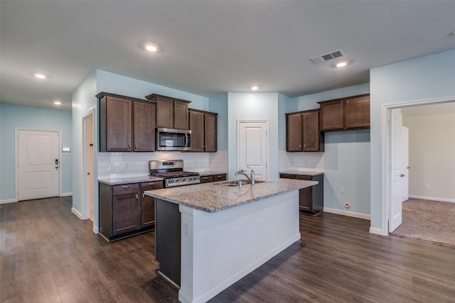 kitchen featuring decorative backsplash, appliances with stainless steel finishes, dark hardwood / wood-style flooring, light stone counters, and an island with sink