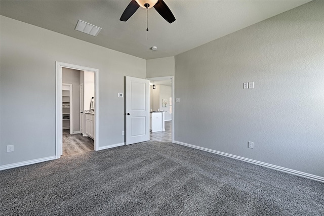 unfurnished bedroom featuring ceiling fan, dark carpet, and ensuite bath