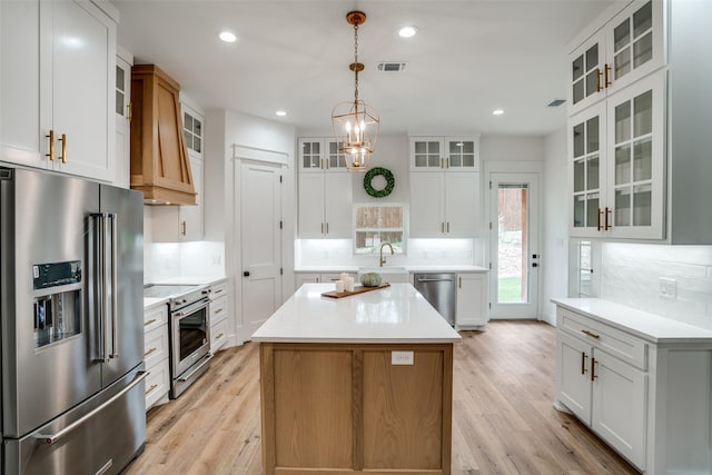 kitchen with a kitchen island, white cabinets, hanging light fixtures, stainless steel appliances, and custom range hood