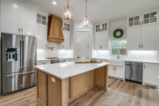 kitchen with premium range hood, white cabinets, sink, appliances with stainless steel finishes, and a kitchen island