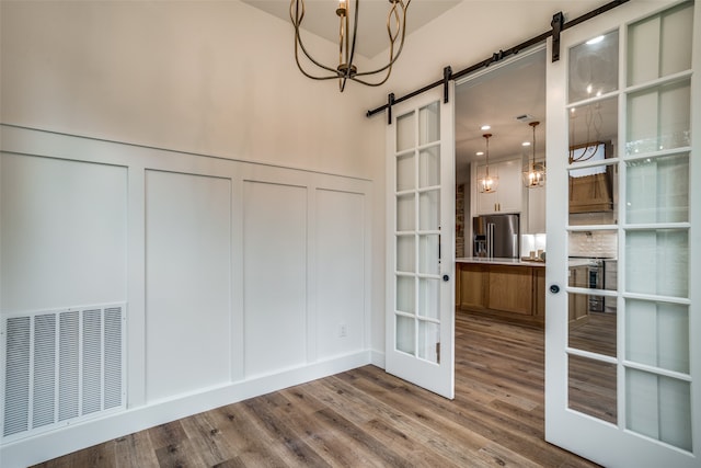 unfurnished dining area featuring french doors, a barn door, hardwood / wood-style flooring, and a notable chandelier