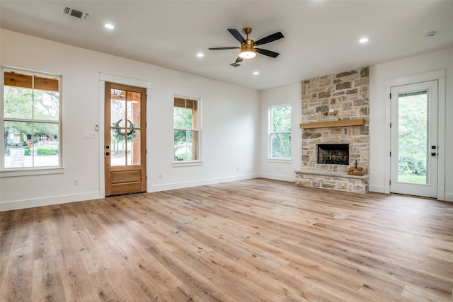 unfurnished living room with light wood-type flooring, a stone fireplace, and ceiling fan