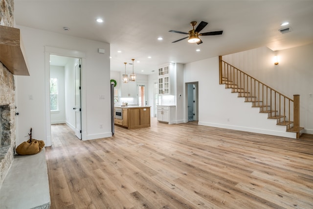 unfurnished living room with ceiling fan with notable chandelier, light hardwood / wood-style floors, and a stone fireplace