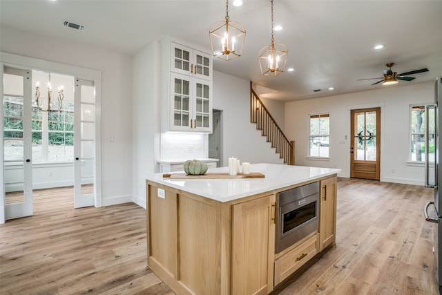 kitchen with light brown cabinetry, stainless steel microwave, a kitchen island, and light hardwood / wood-style floors