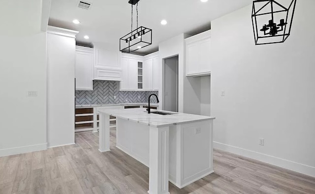 kitchen with white cabinets, light hardwood / wood-style flooring, sink, and an island with sink